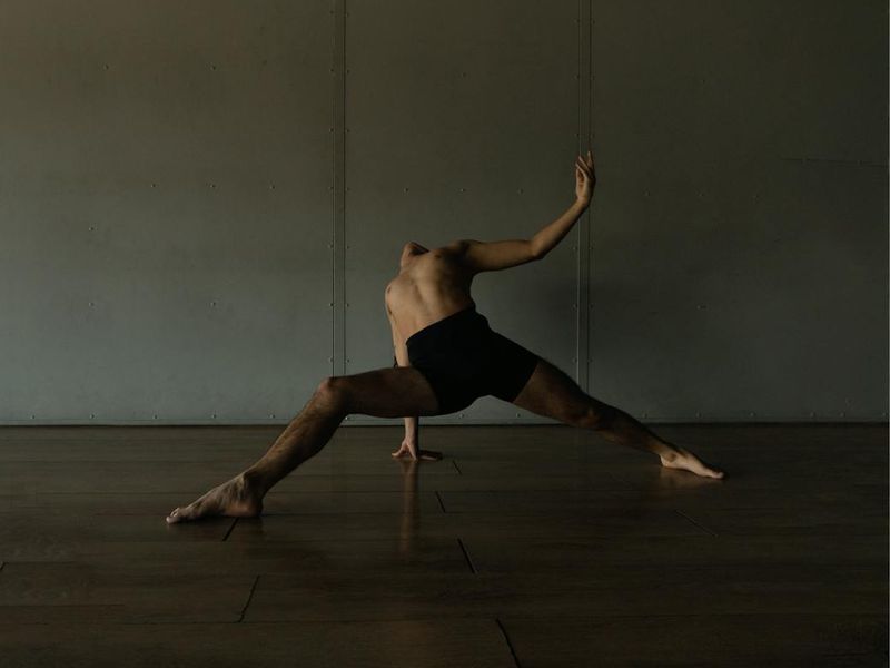 Detailed close-up of a person performing a controlled yoga movement in dark studio